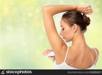 hygiene, bodycare and people concept - beautiful young woman applying antiperspirant or stick deodorant over summer green lights background. woman with antiperspirant deodorant over green. woman with antiperspirant deodorant over green