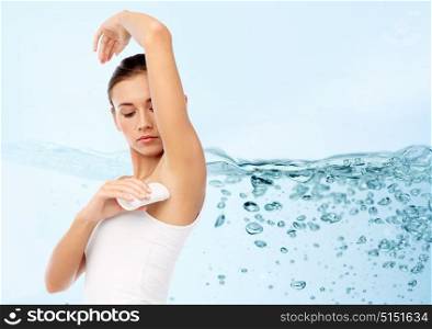 hygiene, bodycare and people concept - beautiful young woman applying antiperspirant or stick deodorant over blue background with water splash and air bubbles. woman with antiperspirant deodorant over blue