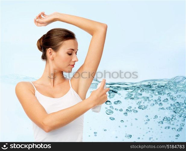 hygiene, bodycare and people concept - beautiful young woman applying antiperspirant or spray deodorant over blue background with water splash and air bubbles. woman with antiperspirant deodorant over blue