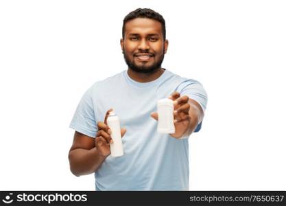 hygiene, grooming and people concept - happy smiling african american man choosing between stick deodorant and antiperspirant spray over white background. african american man with antiperspirant deodorant