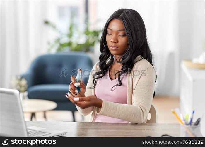 hygiene, health care and safety concept - african american woman spraying antibacterial hand sanitizer at home office. woman spraying hand sanitizer at home office