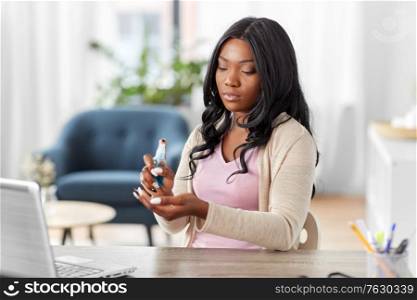 hygiene, health care and safety concept - african american woman spraying antibacterial hand sanitizer at home office. woman spraying hand sanitizer at home office