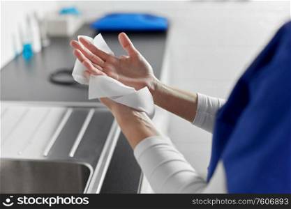 hygiene, health care and safety concept - close up of female doctor or nurse drying hands with paper tissue at hospital. doctor or nurse drying hands with paper tissue