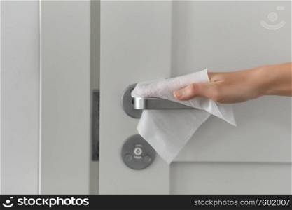 hygiene, health care and safety concept - close up of hand cleaning and disinfecting door handle surface with antiseptic wet wipe. hand cleaning door handle with antiseptic wet wipe