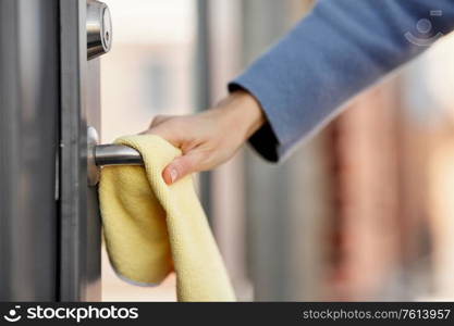 hygiene, health care and safety concept - close up of hand cleaning outdoor door handle surface with microfiber rag. hand cleaning door handle with microfiber rag