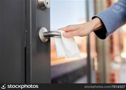 hygiene, health care and safety concept - close up of hand cleaning outdoor door handle surface with paper tissue. hand cleaning door handle with paper tissue