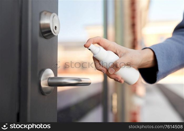 hygiene, health care and safety concept - close up of hand cleaning outdoor door handle surface with disinfectant spray. hand cleaning door handle with disinfectant spray