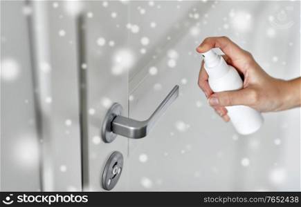 hygiene, health care and safety concept - close up of hand spaying disinfectant or sanitizer to door handle surface in winter over snow. hand spaying disinfectant to door handle surface