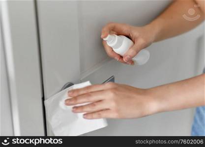 hygiene, health care and safety concept - close up of hands cleaning door handle surface with disinfectant spray and tissue. hand cleaning door handle with disinfectant spray