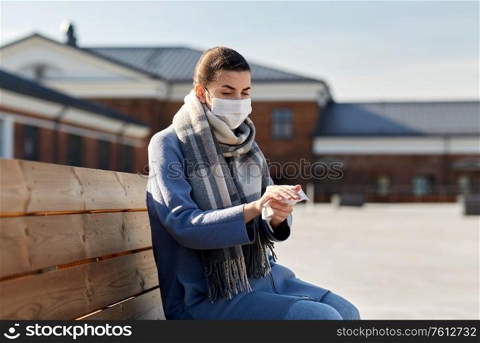 hygiene, health care and safety concept - close up of woman in protective face mask cleaning hands with antiseptic wet wipe on city street. woman in mask cleaning hands with antiseptic wipe