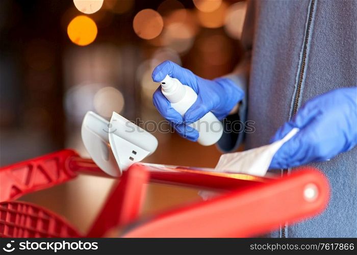 hygiene, health care and safety concept - close up of woman in gloves cleaning outdoor door handle with hand sanitizer and tissue. woman cleaning shopping cart handle with sanitizer