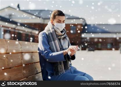 hygiene, health care and safety concept - close up of woman in protective face mask cleaning hands with antiseptic wet wipe on city street over snow. woman in mask cleaning hands with antiseptic wipe