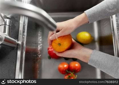 hygiene, health care and safety concept - close up of woman&rsquo;s hands washing fruits and vegetables in kitchen at home. woman washing fruits and vegetables in kitchen