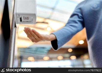 hygiene, health care and safety concept - close up of woman using hand sanitizer from dispenser at shopping mall. close up of woman at dispenser with hand sanitizer