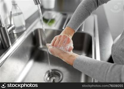 hygiene, health care and safety concept - close up of woman washing hands with liquid soap in kitchen at home. woman washing hands with liquid soap in kitchen
