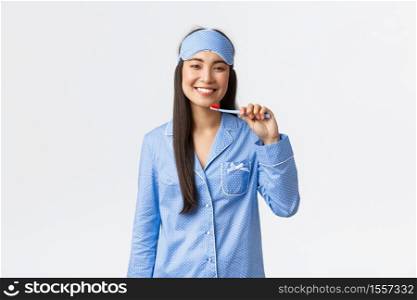 Hygiene, lifestyle and people at home concept. Smiling cheerful asian girl in pajamas and sleeping mask, going to bed, brushing teeth and grinning delighted, whiten smile with toothpaste.. Hygiene, lifestyle and people at home concept. Smiling cheerful asian girl in pajamas and sleeping mask, going to bed, brushing teeth and grinning delighted, whiten smile with toothpaste