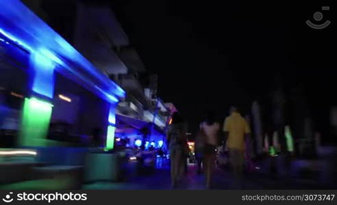 Hyperlapse shot of moving through crowded illuminated streets at night. Passing by hotels, cafes and stores in resort city