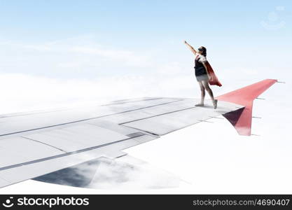 I am a super girl. Powerful super hero kid girl standing on wing of flying airplane