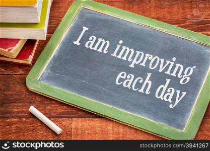 I am improving each day - self development concept or positive affirmation on a slate blackboard with a white chalk and a stack of books against rustic wooden table