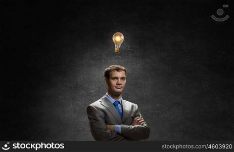 I have an idea. Young confident businessman with arms crossed on chest looking at light bulb