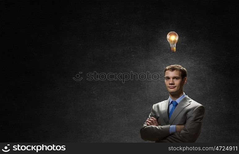 I have an idea. Young confident businessman with arms crossed on chest looking at light bulb