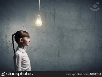 I have bright idea. Side view of girl of school age looking at hanging bulb