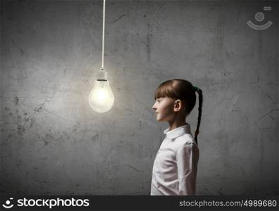 I have bright idea. Side view of girl of school age looking at hanging bulb