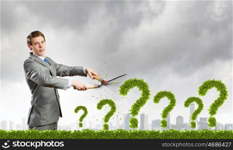 I have question. Young businessman cutting plant shaped like question mark