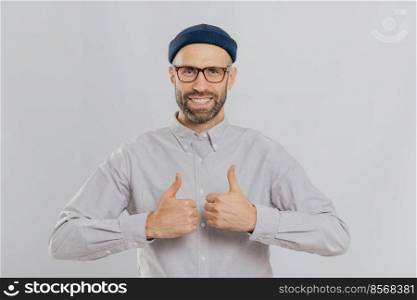 I like this idea  Glad unshaven man raises thumbs up, smiles broadly, satisfied with great choice, has dark stubble, dressed in formal shirt, isolated over white background, approves cool idea