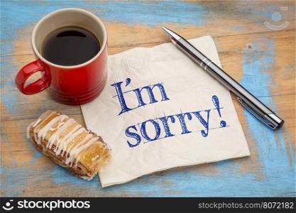 I'm sorry - handwriting on a napkin with a pen,cup of espresso coffee and cookie against grunge painted wood