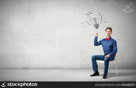 I&rsquo;ve got an idea!. Young funny guy sitting in chair and pointing upwards