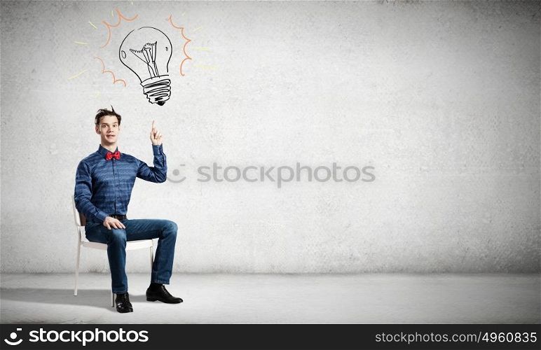 I&rsquo;ve got an idea!. Young funny guy sitting in chair and pointing upwards