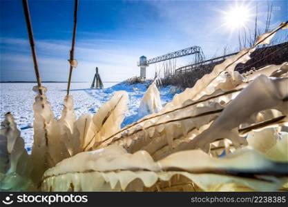 Ice covered plants in freezing lake shore in winter. Chilly winter afternoon at seaside promenade, sunset and frozen bushes. Icicles lit by the sun on the branches.. Breakwater with reed border covered by snow and ice in wintertime