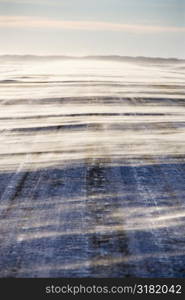 Ice covered road with snow being blown over.