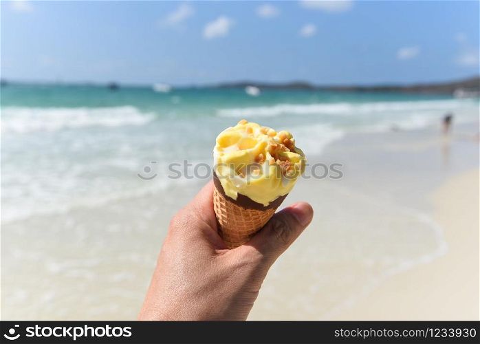Ice cream cone in hand with sea background / Melting ice cream on beach in summer hot weather ocean landscape nature outdoor vacation , Yellow ice cream mango with nuts