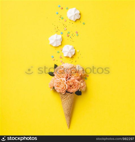 Ice cream cone with pink roses and merengues on yellow background. Summer minimal concept. Flat lay.