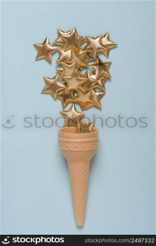 Ice cream cone with shiny golden stars on blue pastel background top view