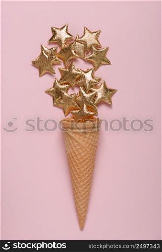 Ice cream cone with shiny golden stars on pink pastel background flatlay