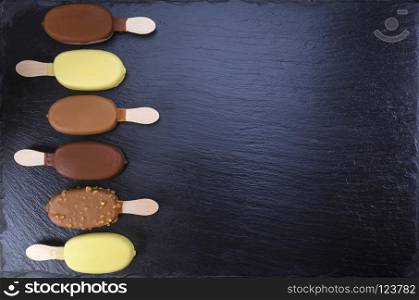 Ice cream on stick covered with chocolate on black stone slate board. Focus on ice cream. Ice cream on stick covered with chocolate on black