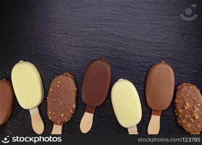 Ice cream on stick covered with chocolate on black stone slate board.. Ice cream on stick covered with chocolate