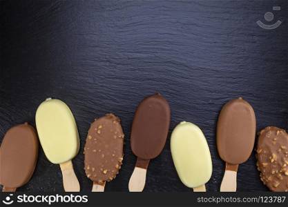Ice cream on stick covered with chocolate on black stone slate board.. Ice cream on stick covered with chocolate on black