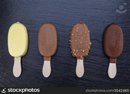 Ice cream on stick covered with chocolate on black stone slate board.. Ice cream on stick covered with chocolate on black slate