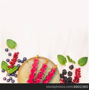 Ice cream pops in plate with summer berries: red currant, blackberries, blueberries and peppermint leaves on white wooden background, top view place for text, frame
