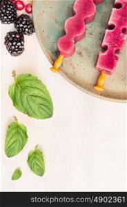 Ice cream pops with summer berries and peppermint leaves on white wooden background, top view, place for text