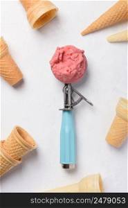 Ice cream scoop with ball of fruit homemade icecream surrounded by empty wafer cones on white table flatlay