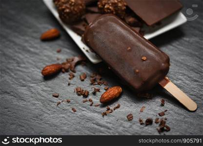 ice cream stick with almonds nut chocolate bar and ball on dark background / ice cream covered chocolate frozen popsicle sweet dessert or snack