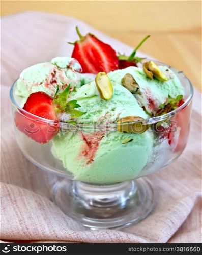 Ice cream strawberry and pistachio in a glass goblet with strawberries and pistachios on a napkin on a wooden board