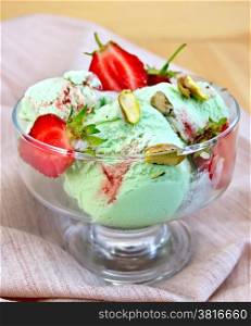 Ice cream strawberry and pistachio in a glass goblet with strawberries and pistachios on a napkin on a wooden board