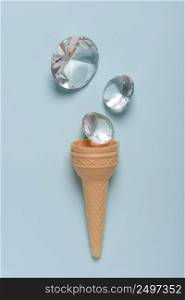 Ice cream wafer cone with shiny gems on blue pastel background top view