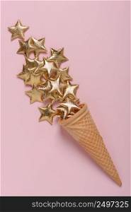 Ice cream wafer cone with shiny gold stars on pink pastel background flatlay
